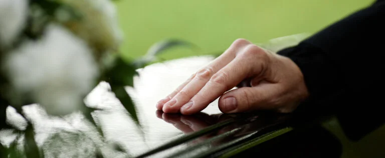 Closeup of womans hand on coffin saying goodbye at outdoor funeral ceremony, copy space