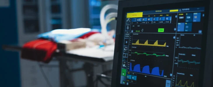 Against the background of dark surgery in the light of a lamp a pet lies on the table and there is a monitor showing the life indicator. After the operation the pet lies under the control of monitors.
