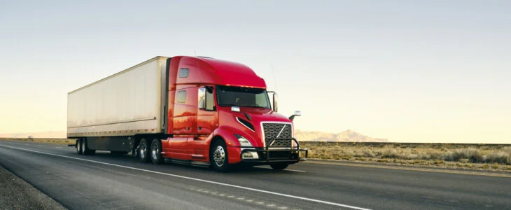 Large semi truck hauling freight on the open highway in the western USA under a morning sky.