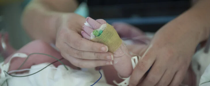 A mother holds the tiny hand of her premature baby in hospital