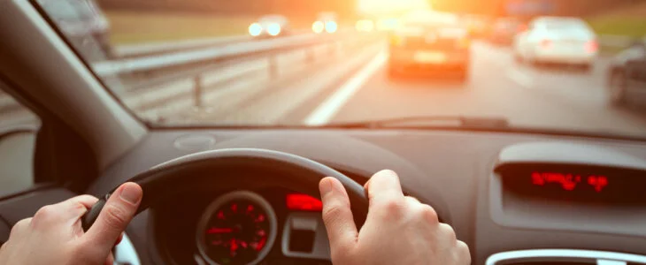 driving on highway road, closeup hands of car driver on steering wheel, road trip at sunset