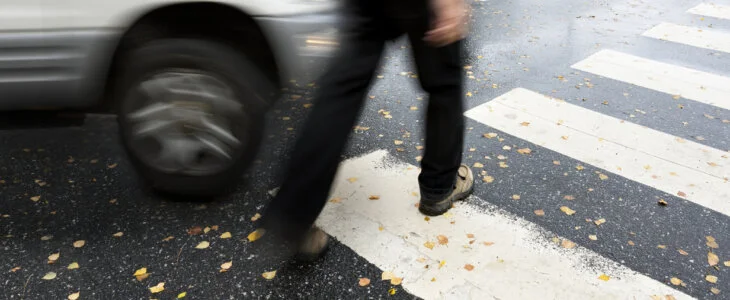 Man on pedestrian crossing in autumn, in danger of being hit by car